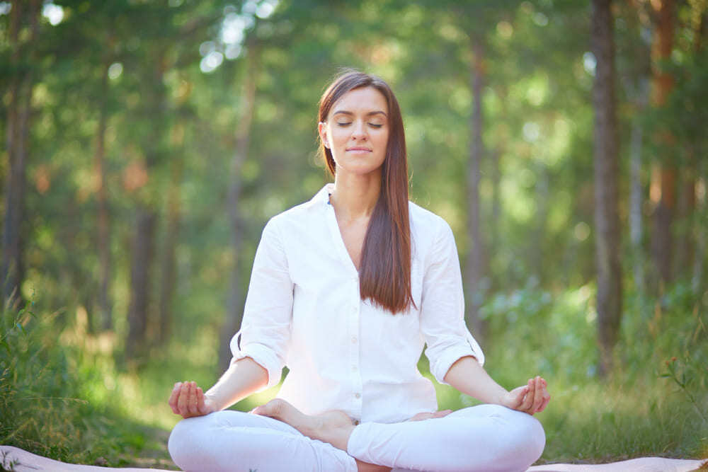 Femme qui pratique la méditation de pleine conscience en forêt en été.