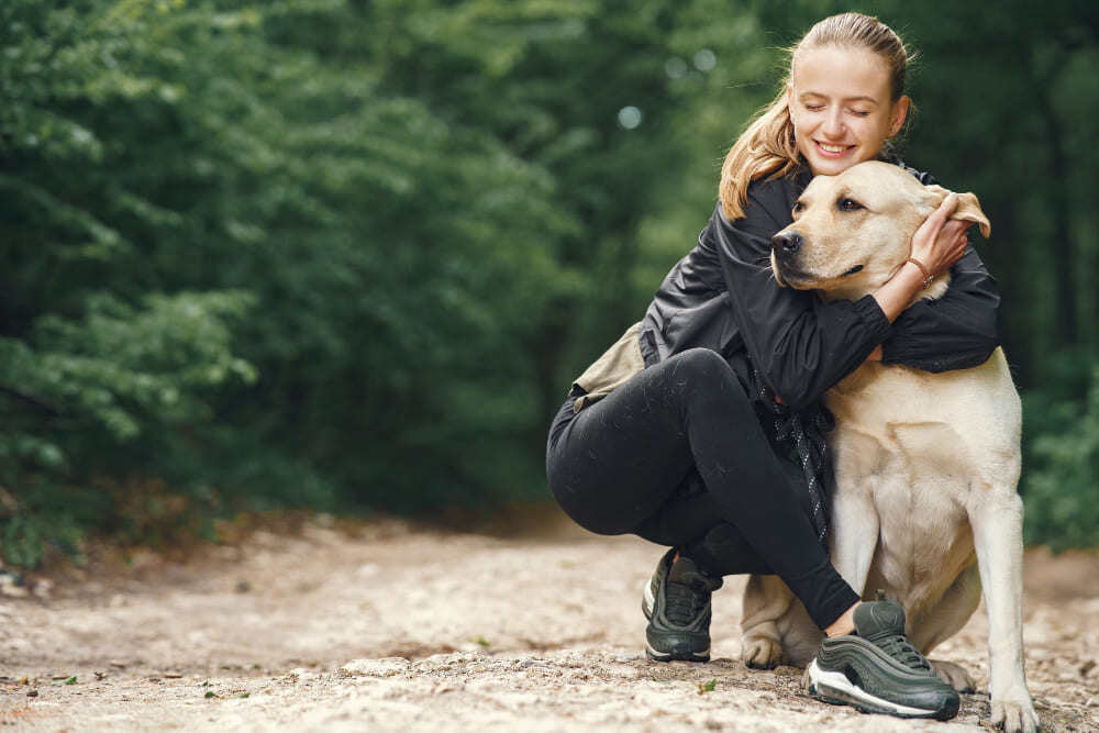 Une femme faisant un câlin à son chien dans une forêt après une promenade.