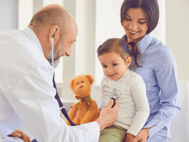 Pédiatre qui examine une enfant avec sa mère qui est derrière avec elle
