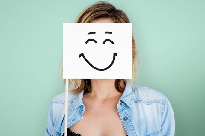 Femme qui porte un panneau devant elle avec un smiley qui sourit, elle pratique la psychologie positive au quotidien.