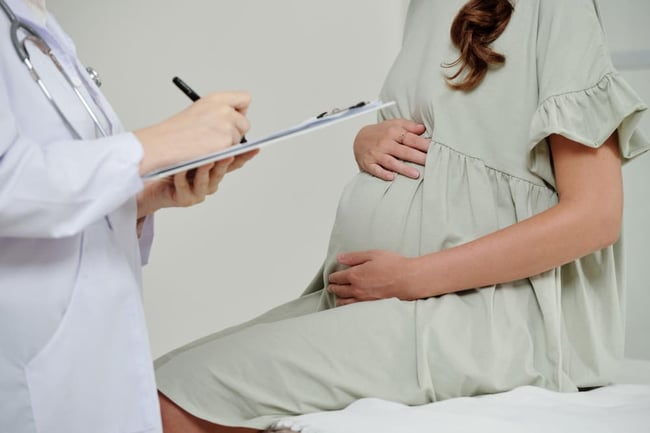 Femme enceinte qui tient son ventre et qui consulte son médecin pour connaître la cause de ses nausées.