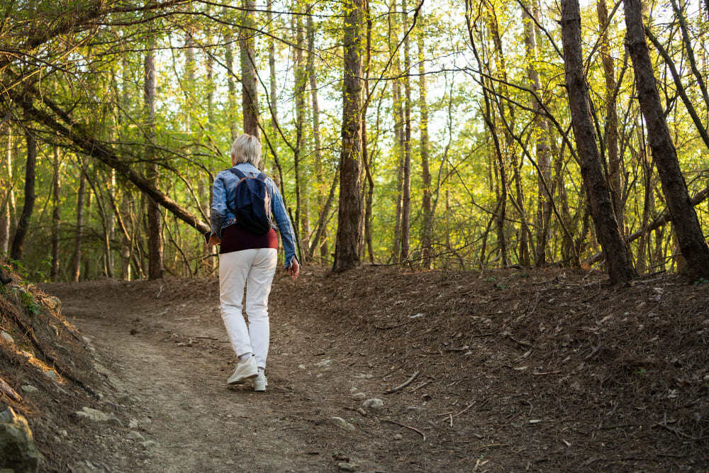 Personne âgée marchant dans une forêt en pratiquant l'écothérapie.