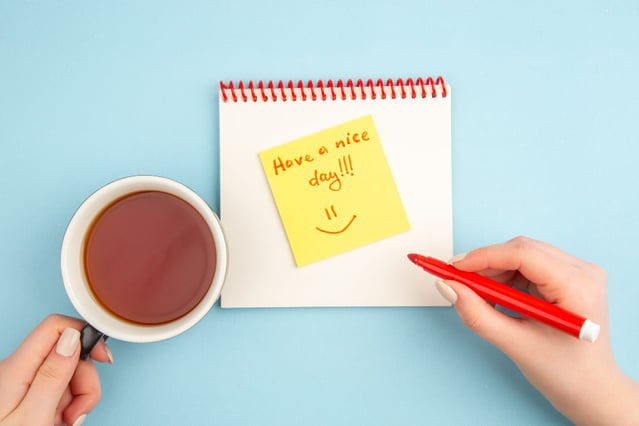 Femme qui tient sa tasse de café et qui écrit sur un post-it un mot positif pour bien débuter la semaine.