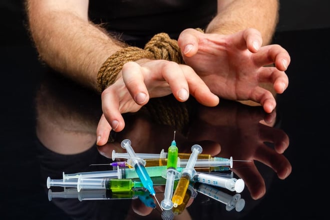 Mains attachées par une corde dirigées vers des drogues injectables en seringues.