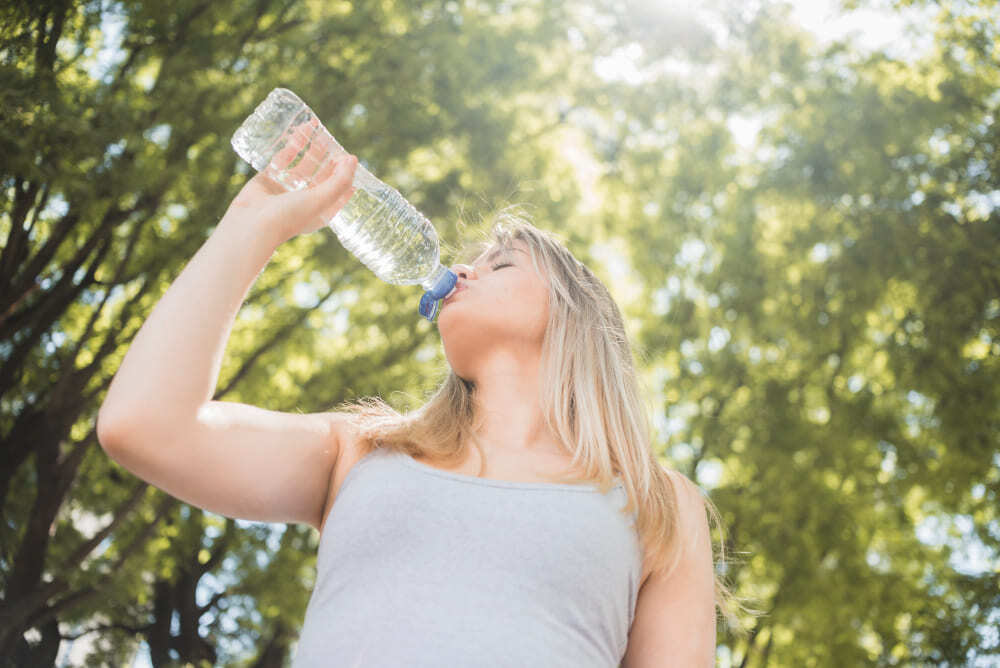Femme qui boit de l'eau en bouteille contaminée par des microplastiques