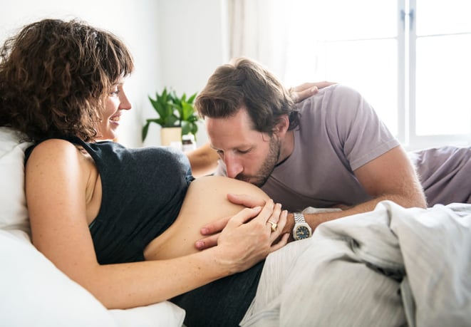 Homme embrassant le ventre de sa femme enceinte pour créer un lien avec l'enfant à naître.