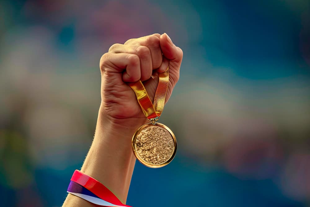 Main qui tient une médaille d'or JO 2024 