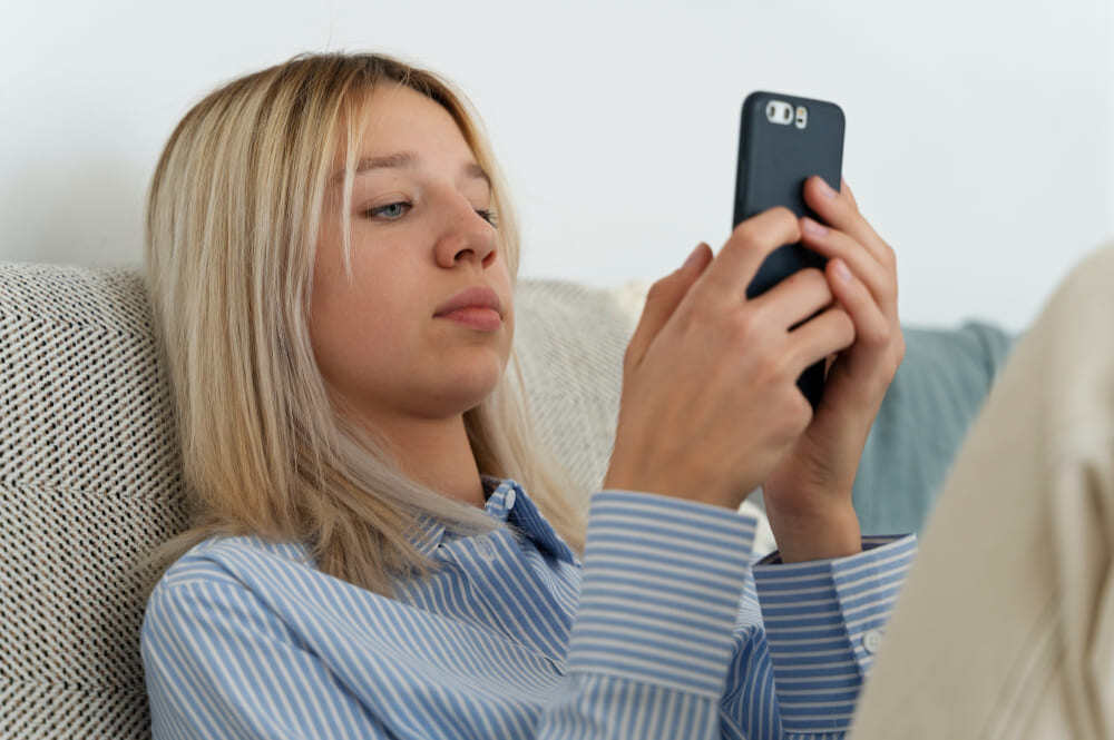 Femme posée sur un canapé en train d'utiliser son téléphone.