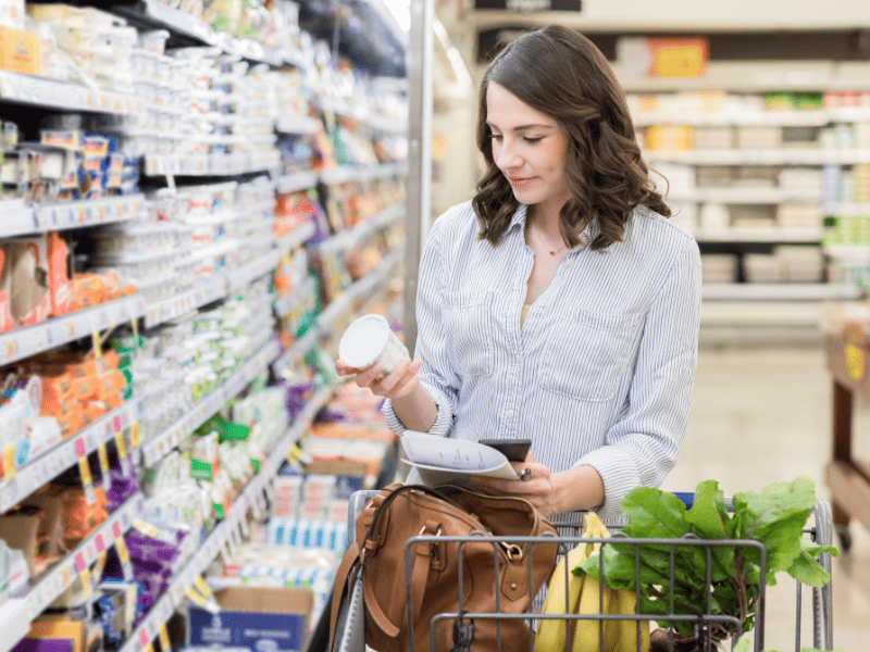 Femme regardant la composition alimentaire d'une crème en faisant ses courses.