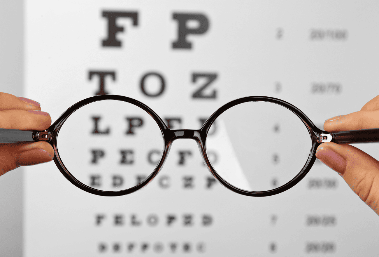 Personne tenant une paire de lunettes avec une correction pour regarder les lettres affichées derrière.