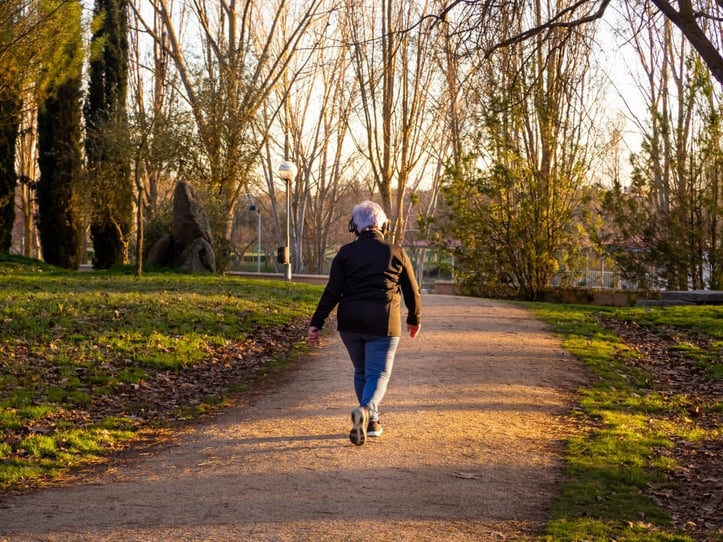 Femme âgée qui marche dans un parc sur un sentier avec de la musique.