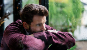 Homme qui se sent seul observant par la fenêtre. La solitude est propre à chacun.