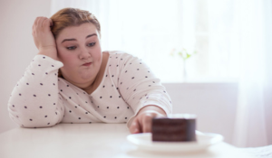 Femme en surpoids devant un dessert au chocolat riche en sucre.